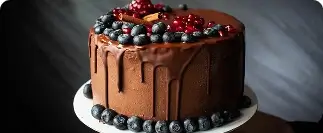 Chocolate drip cake topped with fresh blueberries, pomegranates, and raspberries