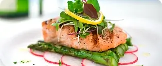 Grilled salmon fillet with asparagus, mixed greens, and lemon garnish on a white plate