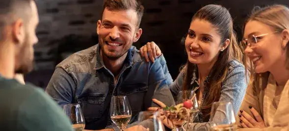 Group of smiling friends enjoying wine and charcuterie at a cozy indoor restaurant table, sharing laughs and conversation in a warm, relaxed atmosphere.
