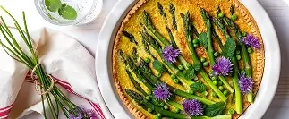 Asparagus and pea quiche with purple flowers in golden pastry crust