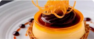 Small round orange dessert with orange tuile garnish and caramel sauce drizzle