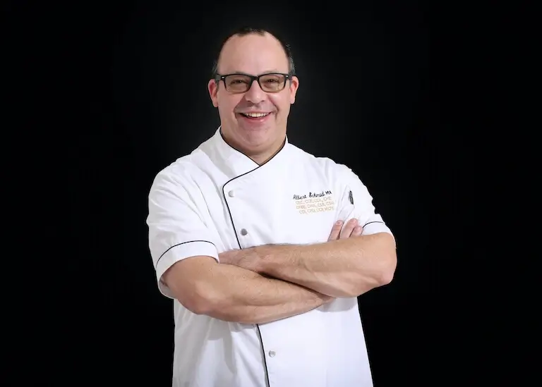 Portrait of a smiling Chef Instructor in chef whites in a teaching kitchen.