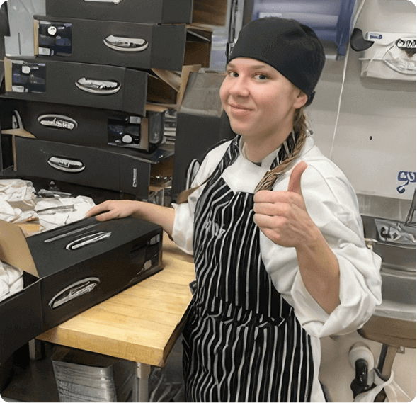 Escoffier culinary student in chef whites giving a thumbs up in a commercial kitchen