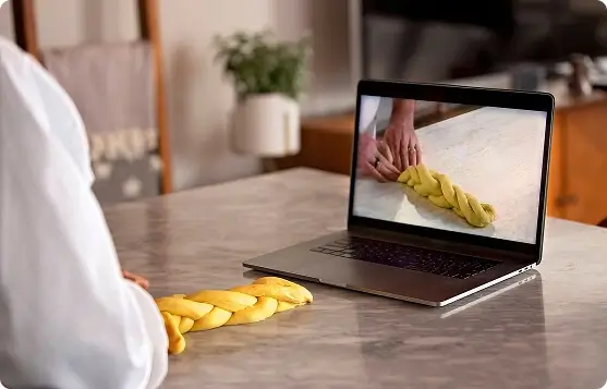 Escoffier culinary student following a braided dough lesson on a laptop at the kitchen counter
