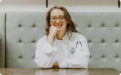 Escoffier graduate Cassie Wallace smiling at a table in a chef uniform.