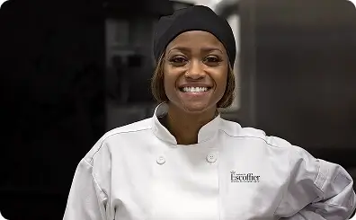 Escoffier culinary graduate Tiffany Moore in a chef coat smiling in a professional kitchen