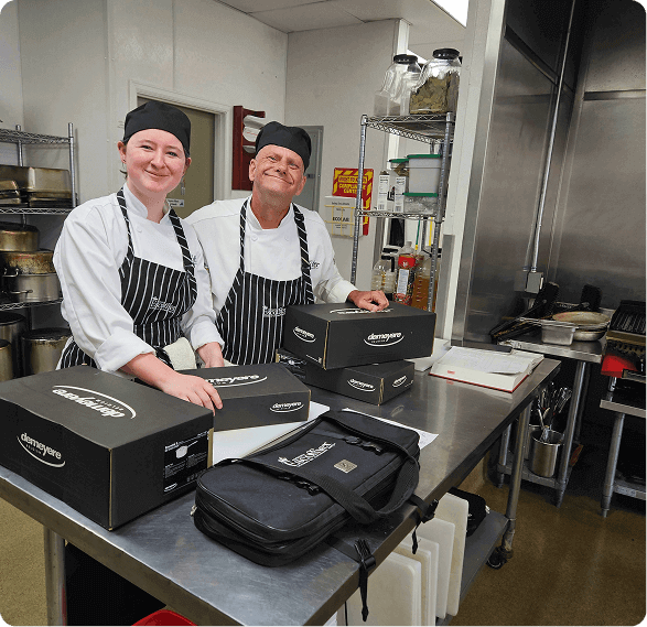 Two escoffier culinary students smiling with Zwilling knife kits in an Escoffier training kitchen