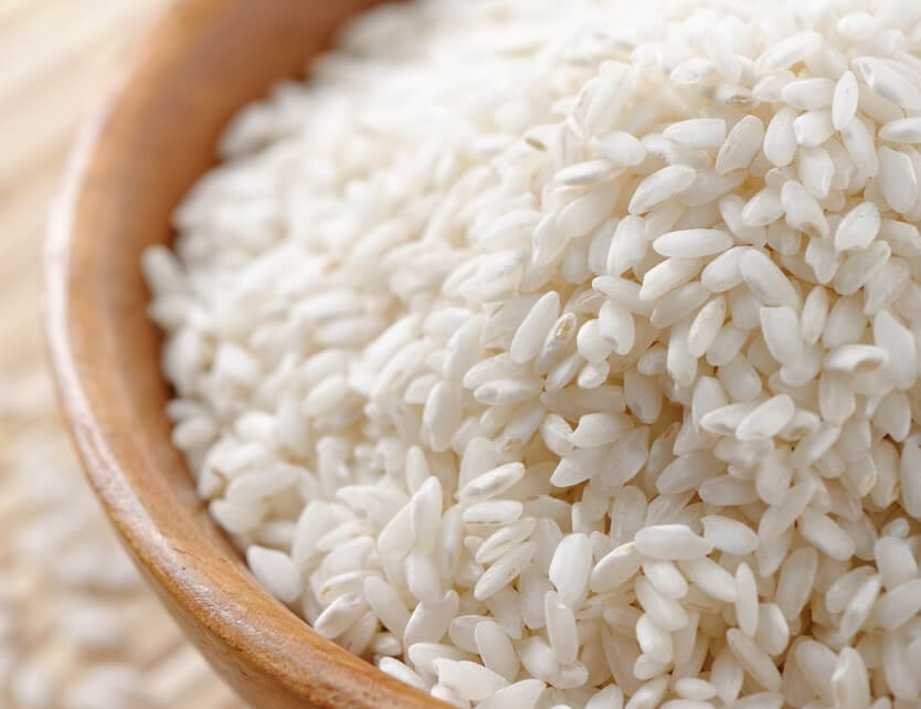 A wooden bowl filled with raw Carnaroli rice, close-up of short, pearly grains.