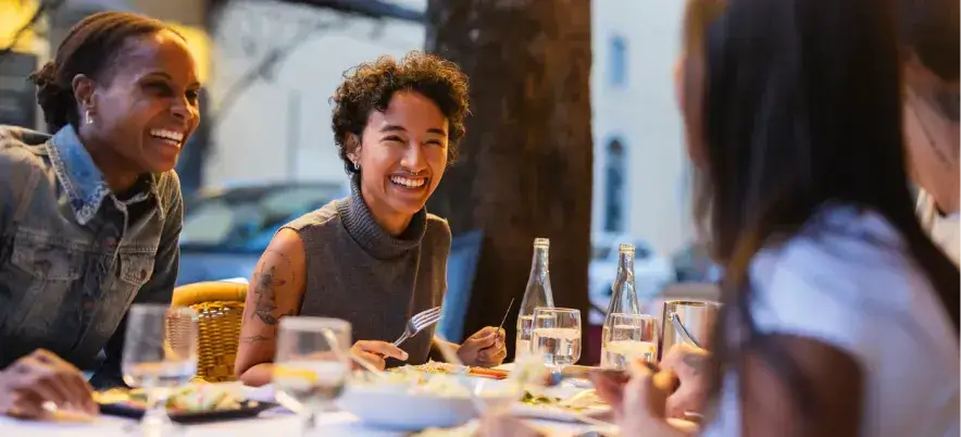 Friends dining at an outdoor restaurant in the evening, smiling and sharing a meal.