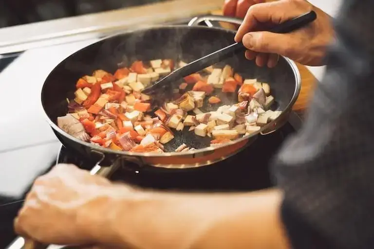 Private chef pan-frying tofu and vegetables in a home kitchen setting.