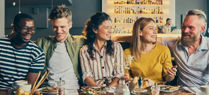Group of friends laughing together at a restaurant brunch table with food and drinks.