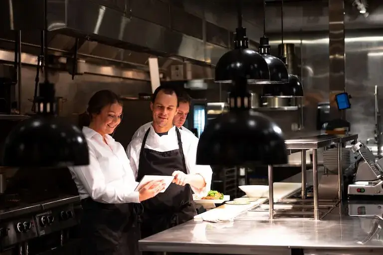 Chef and team reviewing a digital tablet together in a professional kitchen during service.