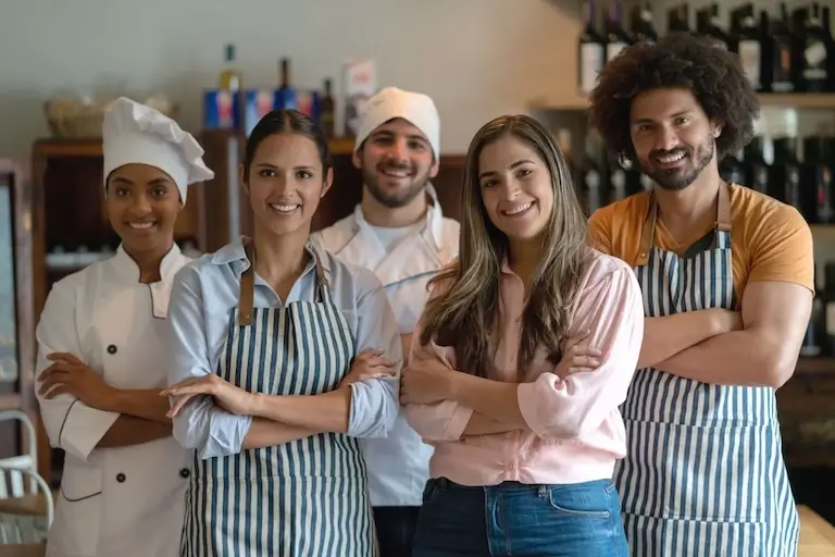Group of chefs and cooks standing together and smiling in a restaurant kitchen.