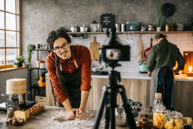 Chef filming a cooking video while kneading dough on a work surface.