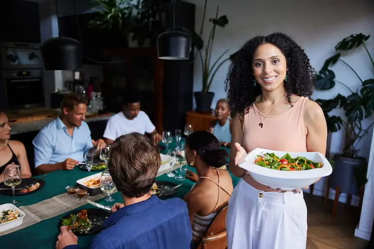 Person serving salad to guests at a dinner table.