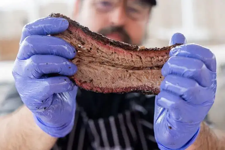 Chef in blue gloves holding perfectly smoked brisket.