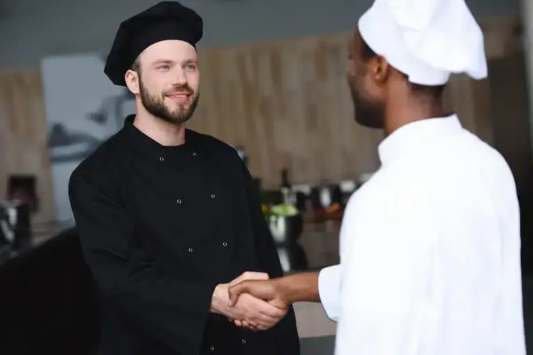 Two chefs shaking hands in a professional kitchen.