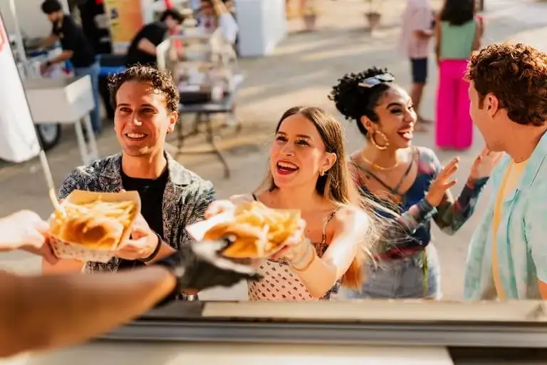 People smiling and receiving food from a food truck at an outdoor festival.