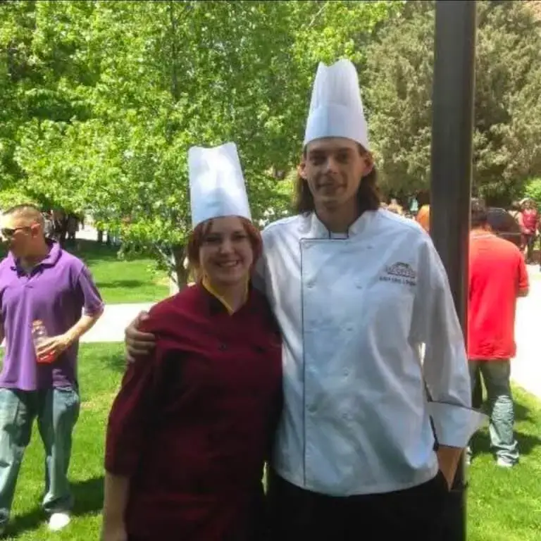 Ellen Doerr and one of her Chef Instructors in chef's coats and toques outdoors after Escoffier Boulder’s graduation ceremony.