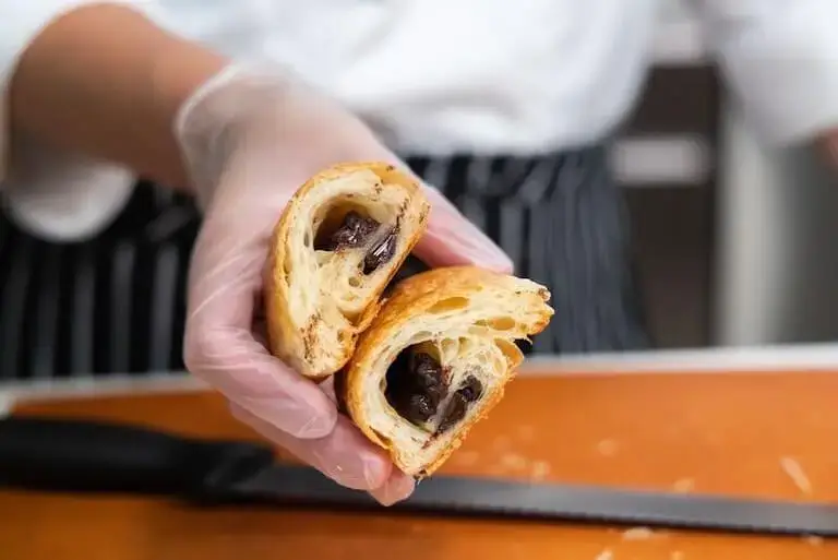 Hand holding a sliced laminated pastry showing flaky layers and chocolate filling