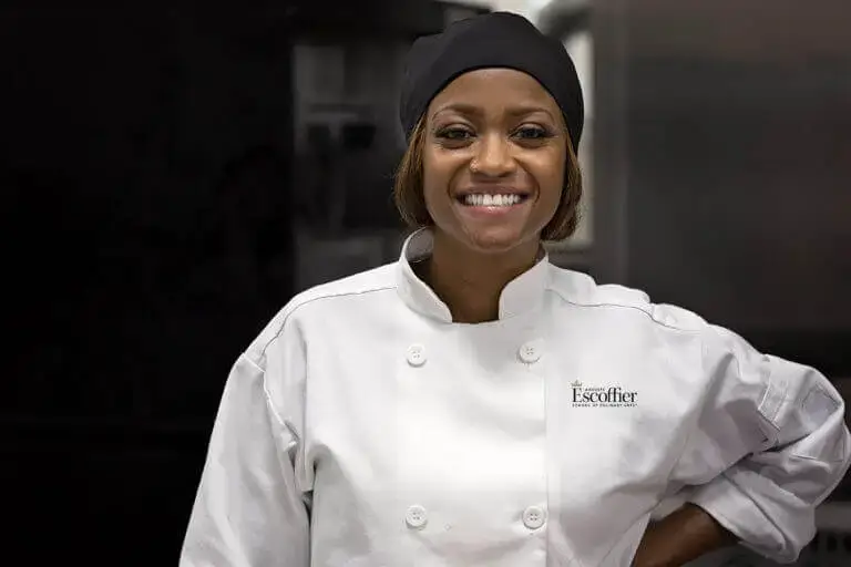 Tiffany Moore, U.S. Army veteran, smiling in a white Escoffier chef's coat and black head covering