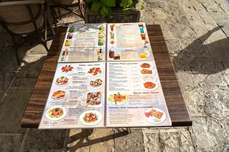 Restaurant menu with colorful food photos showing strategic layout of dishes, drinks, and pricing on outdoor table