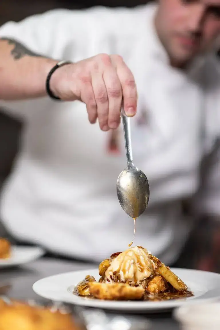 Chef finishing a plated dessert with sauce in a professional kitchen.