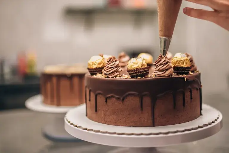 Pastry chef piping frosting onto a chocolate cake.