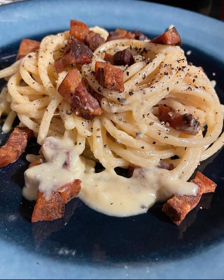 Plate of spaghetti carbonara with crispy pancetta, creamy sauce, and cracked black pepper.