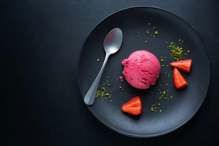 Strawberry ice cream on a black plate with garnish