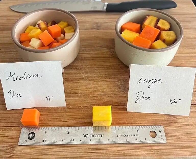 Two bowls of diced carrots and potatoes in medium and large cuts, with handwritten measurement labels and a ruler on a wooden cutting board.