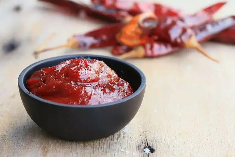 A bowl of thick red gochujang paste with dried red chili peppers in the background.