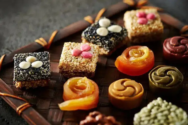 Assortment of Korean sweets including sesame squares and colorful molded confections on a tray.