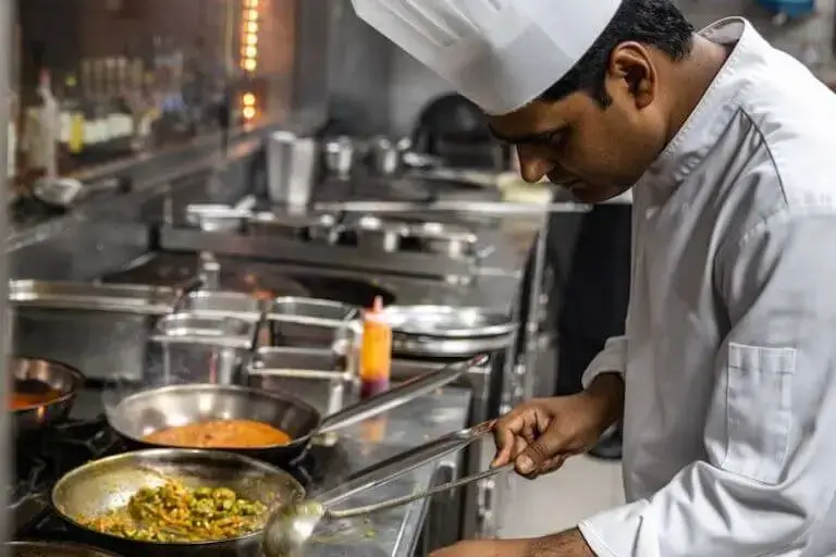 Chef cooking with multiple pans on a commercial stove in a professional kitchen.