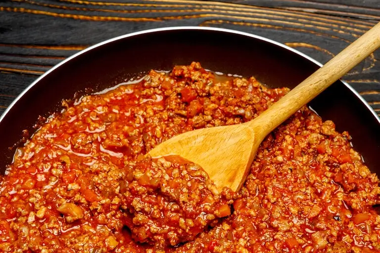 bolognese sauce cooking in a pan with visible softened vegetables and tomato base.