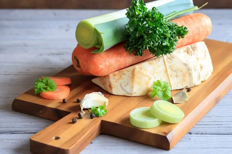 leek, celeriac root, carrot, and herbs arranged on a cutting board for German soup base