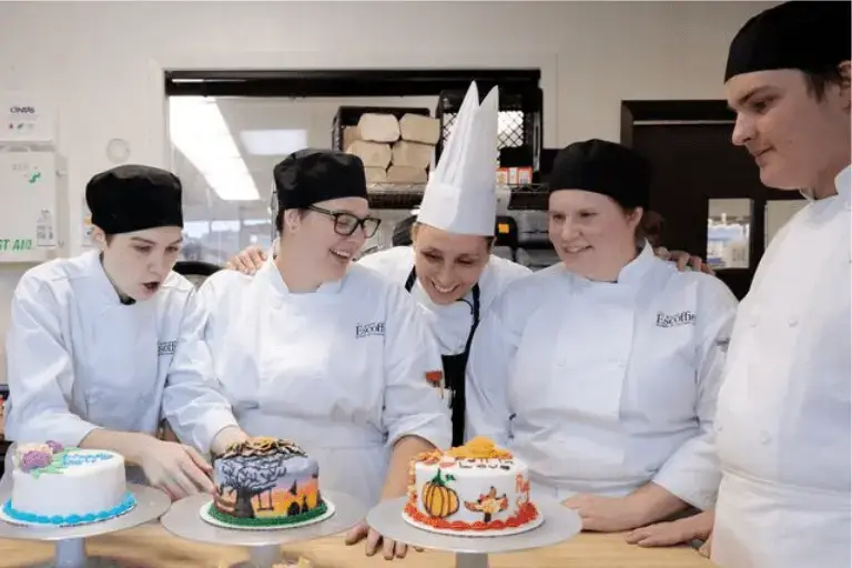 Escoffier culinary students gathered around a display of decorated cakes they created during a baking and pastry session at the Austin campus