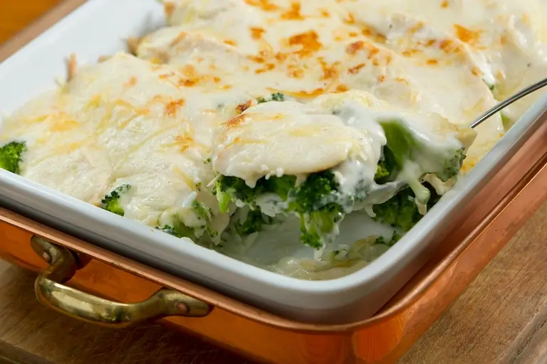 Broccoli gratin covered with creamy melted cheese and browned lightly on top in a white baking dish.