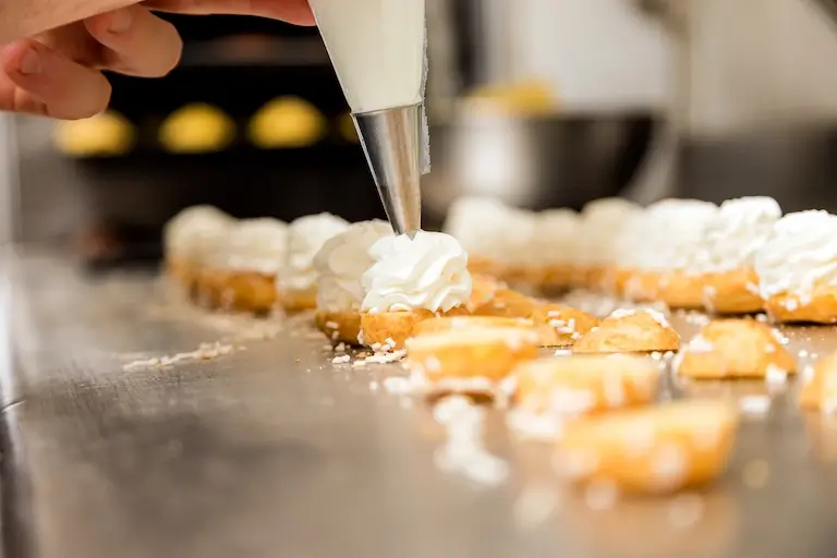 Close-up of a pastry bag piping swirls of cream onto small pastries.