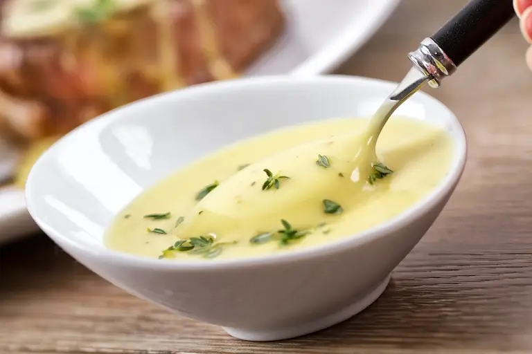 Creamy béarnaise sauce garnished with fresh herbs in a white bowl.