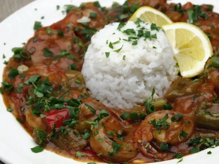 Shrimp in a tomato-based Creole sauce served with white rice, lemon wedges, and chopped herbs.