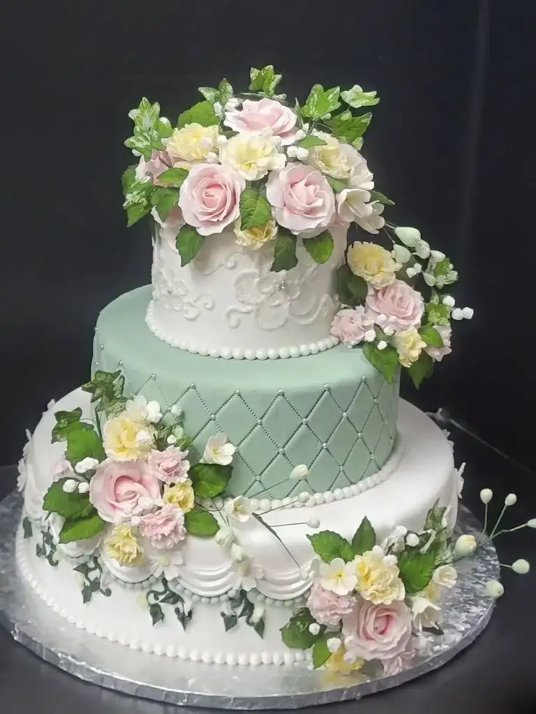 Three-tier wedding cake created by Escoffier Austin campus students with sage green ombre piping and pink and cream sugar flower cascade.