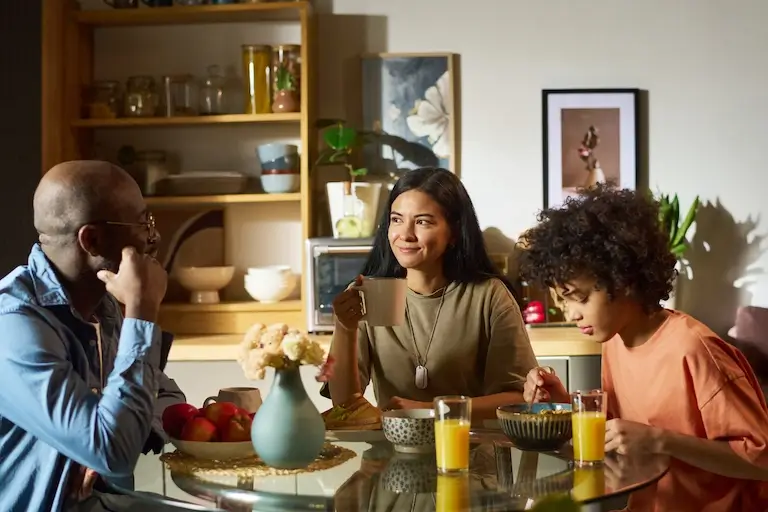 A family of three sitting together at a dining table in conversation, with a child and two adults in a warm home setting.