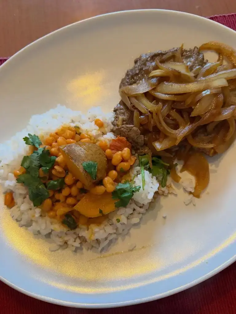 A plated dish of rice topped with a curry and garnished with fresh herbs, prepared by Escoffier graduate Luis R. as part of a cooking assignment.
