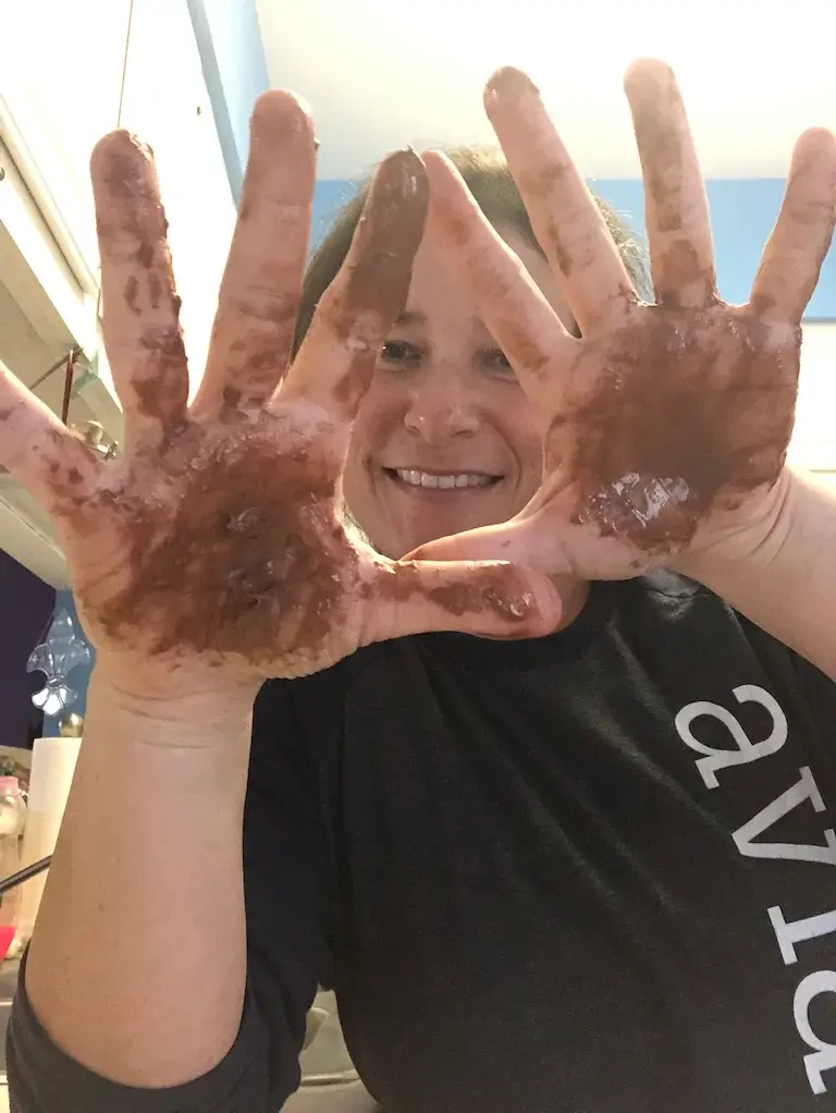 Person smiling and holding up both hands covered in melted chocolate.