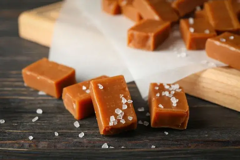 Squares of golden-brown caramel topped with coarse salt crystals on a dark wooden surface.