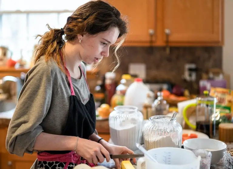 Young woman cutting butter into a mixing bowl while baking in her home kitchen.