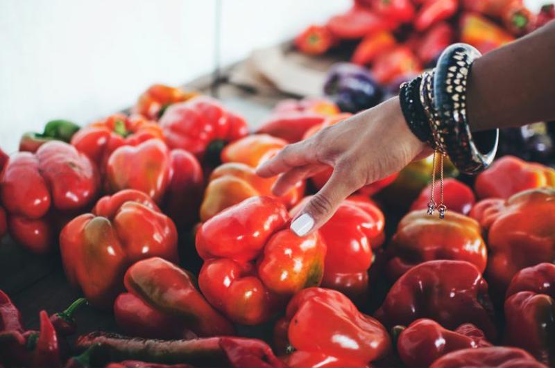 A hand reaches for a red bell pepper from a stand.