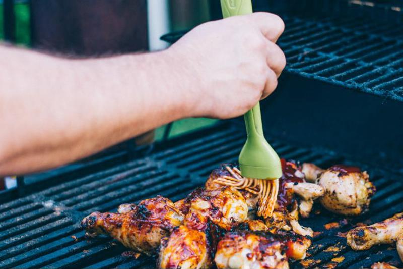 A cook brushes seasoning on chicken on the grill.
