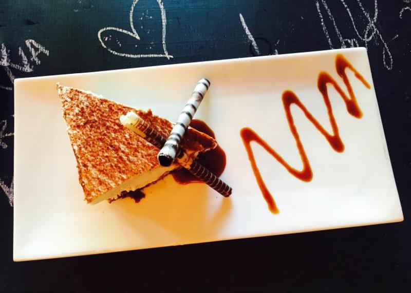 A chocolate pastry is carefully plated, complemented by shaved chocolate and a chocolate drizzle.